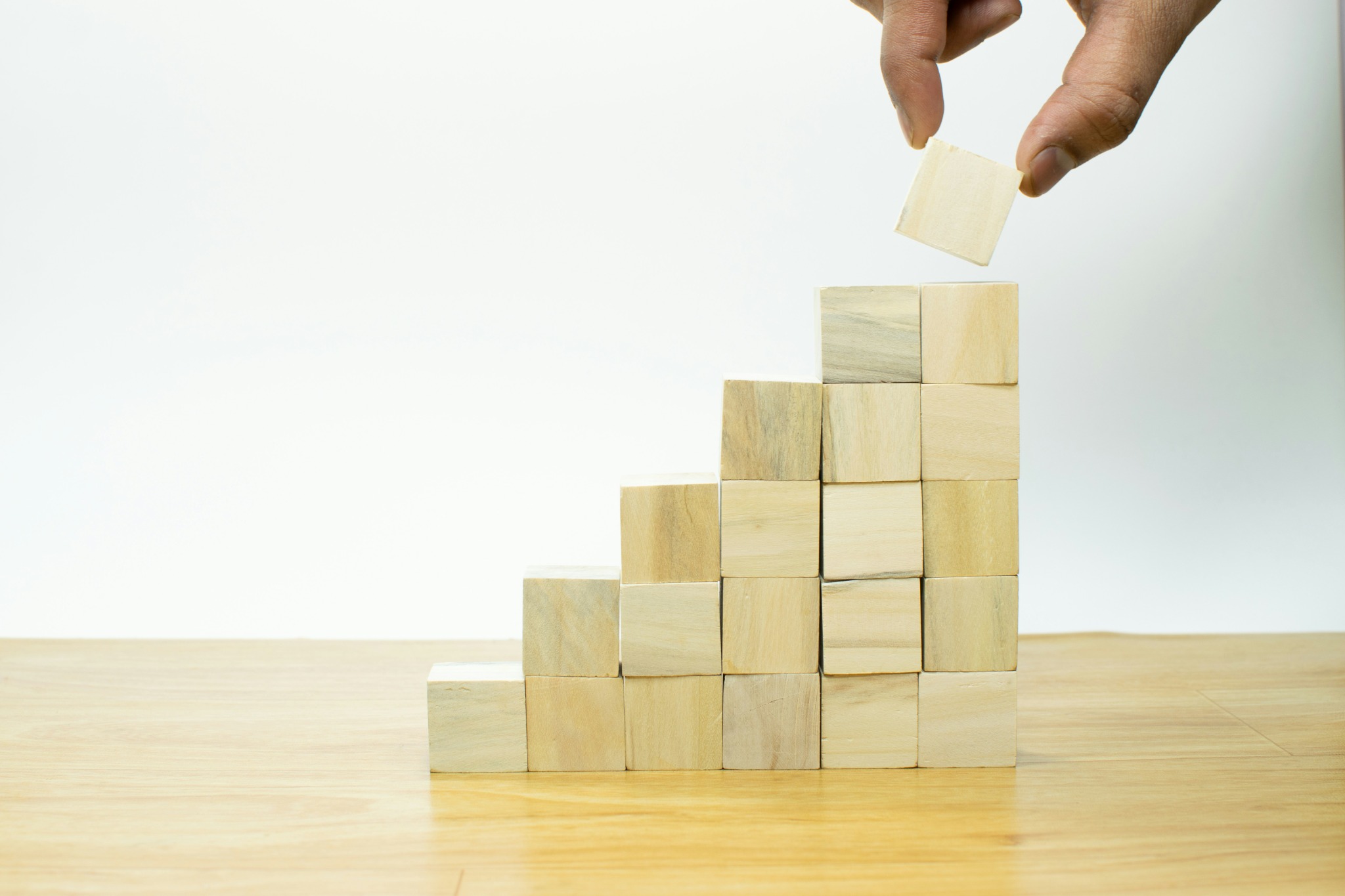 A hand adding a wooden block to a rising staircase
